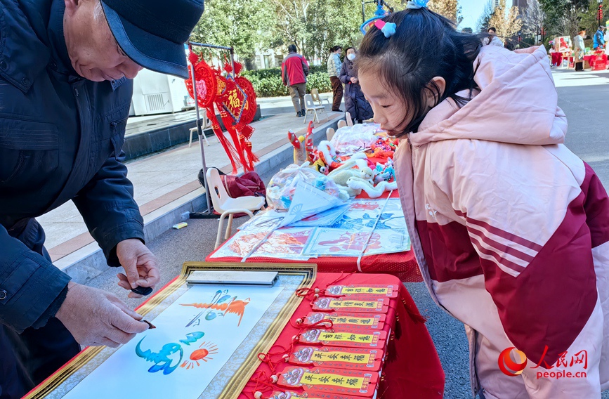 民间花鸟字传承人高景文正在创作“平安幸福”，吸引了小朋友驻足观看。人民网 侯琳琳摄